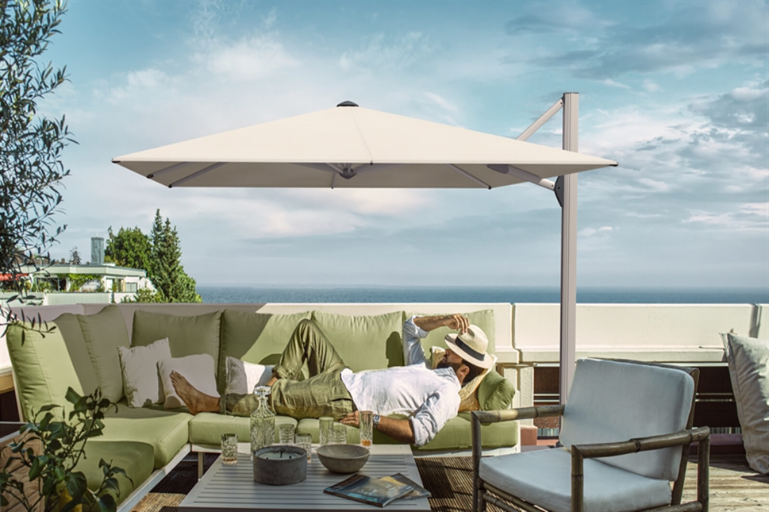 man lying on green outdoor sofa underneath white umbrellas overlooking the ocean