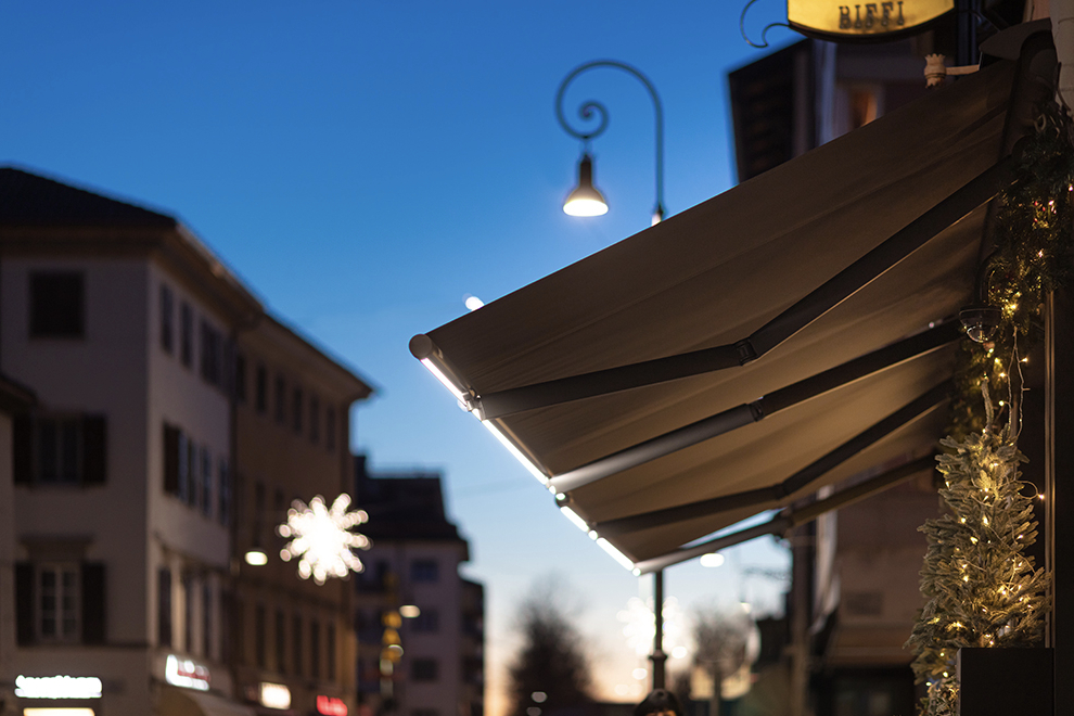 A wall mounted awning above a restaurant patio with integrated lighting on the front bar A wall mounted awning above a restaurant patio with integrated lighting on the front bar